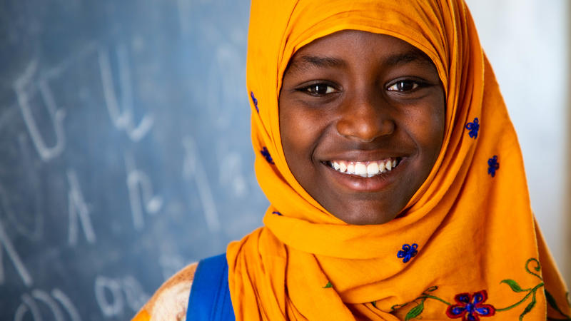 Girl in headscarf standing in front of chalkboard