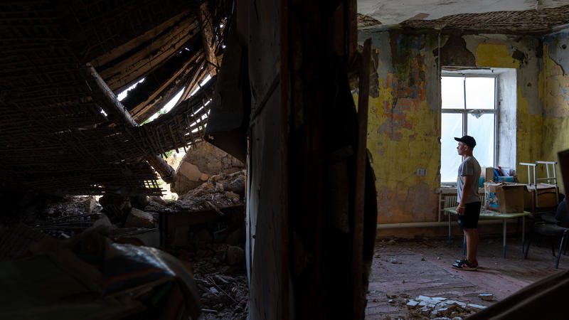 Young Ukrainian teenager standing in ruins of his destroyed school
