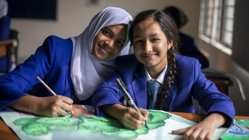 Two girls sit at classroom desk look up smiling
